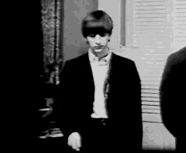 a black and white photo of a young man in a suit standing next to a window .