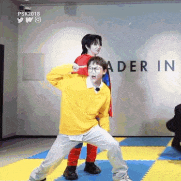 a man in a yellow sweater is standing next to a man in a red cape in front of a wall that says ader