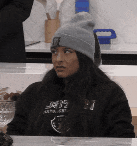 a woman wearing a beanie and a sweatshirt that says massachusetts sits at a table