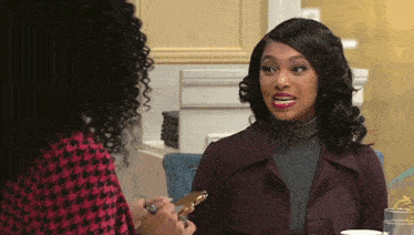 two women are sitting at a table talking to each other and one is holding a piece of cake .