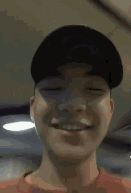 a young man wearing a hat and a red shirt smiles with his eyes closed