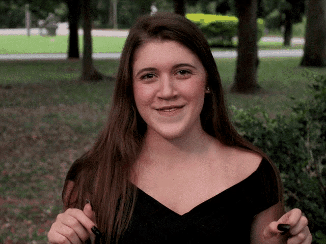 a woman in a black dress is standing in a park