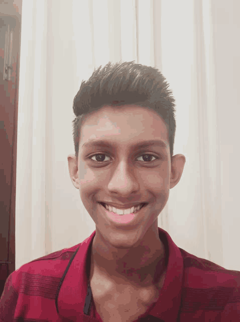 a young man wearing a red striped shirt is smiling for the camera