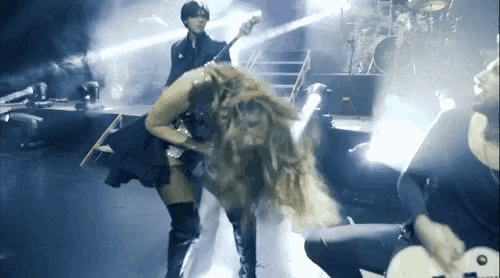 a woman is playing a guitar on a stage with a band behind her