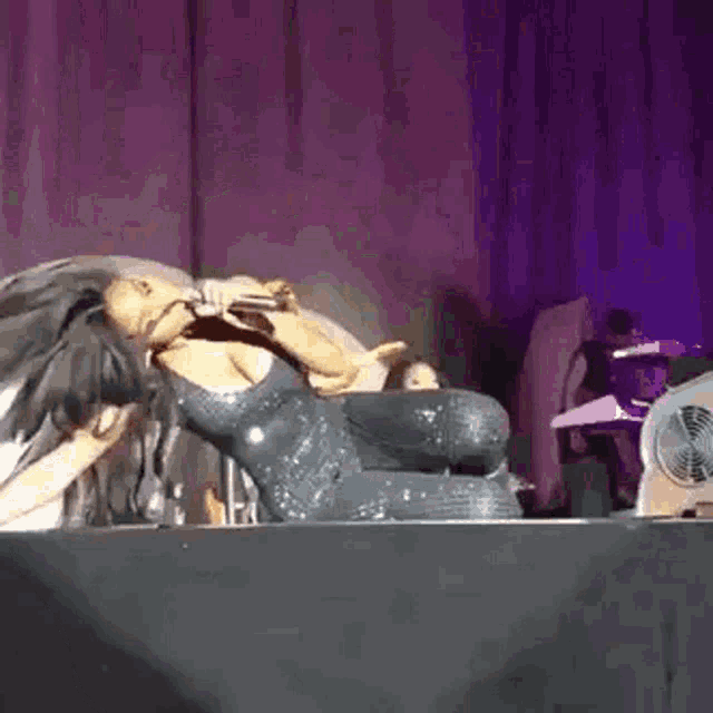 a woman is laying on a stage holding a microphone and singing into it .