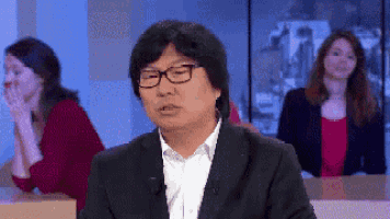 a man wearing glasses is sitting in front of a group of women .
