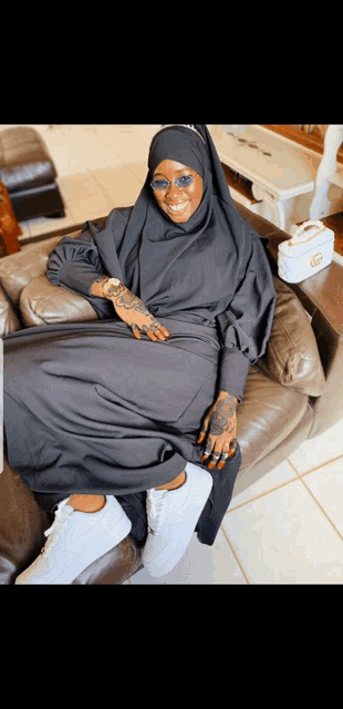 a woman wearing a black hijab and sunglasses is sitting on a couch