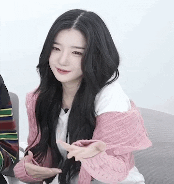 a young woman with long black hair is wearing a pink sweater and a white shirt .