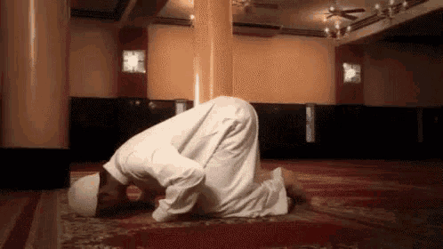 a man in a white robe is kneeling down in a mosque and praying .