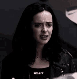 a woman in a black leather jacket is talking to a man in a dark room .