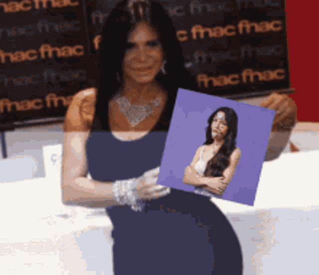 a woman in a blue dress holds a picture of a woman in front of a sign that says fnac