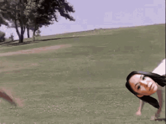 a woman is crawling on the grass in a park with trees in the background .