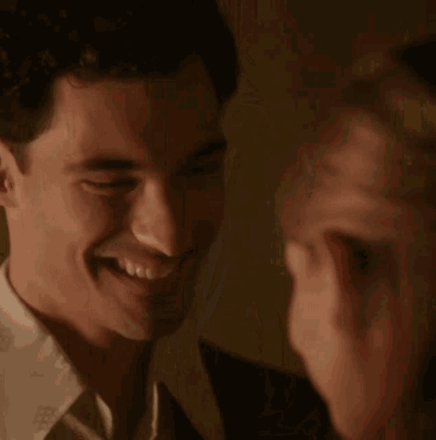 a man in a suit and white shirt is smiling at a woman in a dark room .