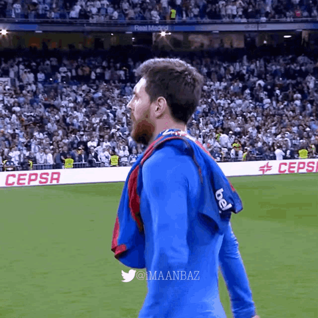 a man in a blue shirt stands on a soccer field in front of a sign that says pepsi