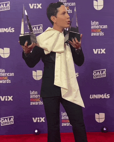 a woman holds up two trophies in front of a wall that says gala vision
