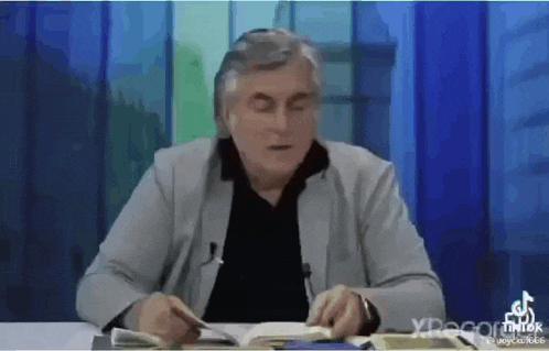 a man is sitting at a table with a book in his hands .