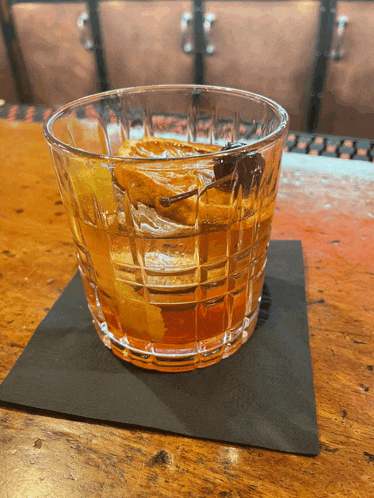 a glass of whiskey sits on a black napkin on a wooden bar