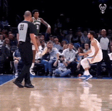 a basketball player is jumping in the air while a referee watches during a game .