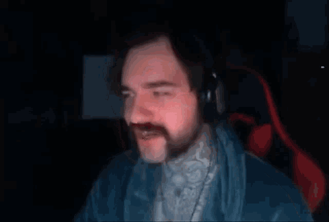 a man with a mustache and headphones is sitting in a chair in a dark room .