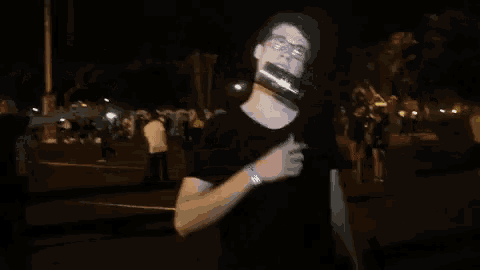 a man in a black shirt has a bottle on his face and is pointing at it
