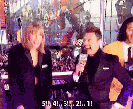 a man in a suit is talking into a microphone while a woman stands behind him with a toy sign behind them