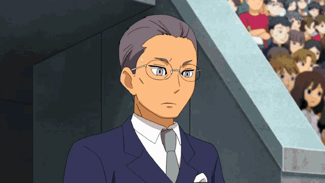 a man wearing glasses and a suit stands in front of a crowd
