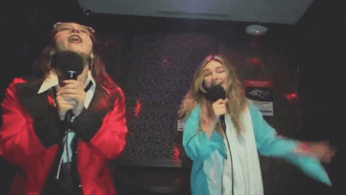 two women singing into microphones in front of a sign that says " no smoking "