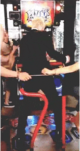 a group of people are playing a video game in an arcade while a man is standing on a treadmill .