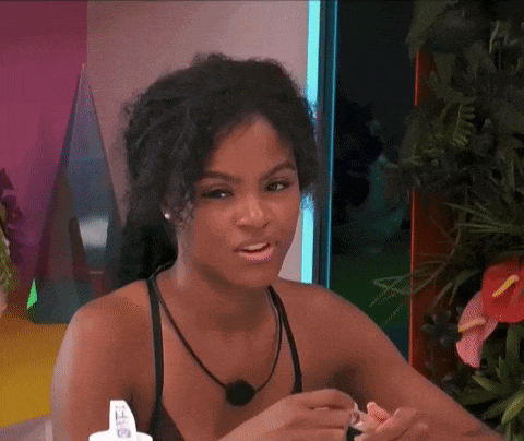 a woman in a black tank top is sitting at a table with a bottle of lotion in her hand .
