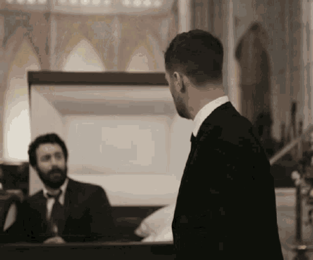 a man in a suit and tie stands next to a coffin