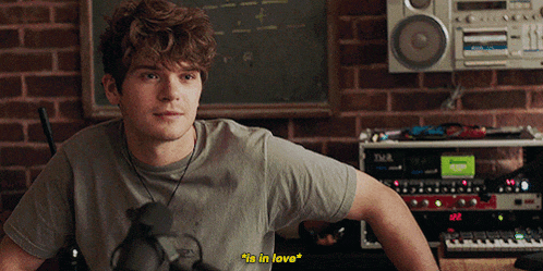 a man in a grey shirt says " in love " in front of a boombox