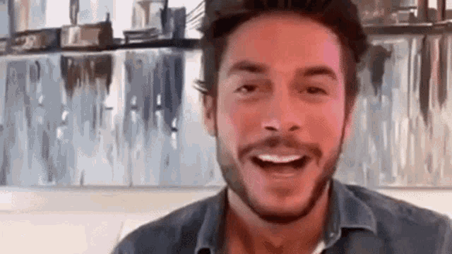 a man with a beard is smiling and looking at the camera while sitting on a couch .