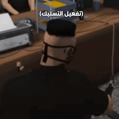 a man wearing glasses and a mask is standing in front of a desk with arabic writing on it ..