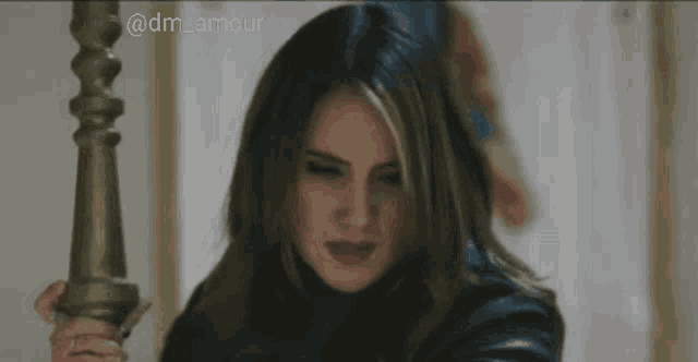 a woman in a black jacket is holding a gold pole with the hashtag @dm_amour on the bottom