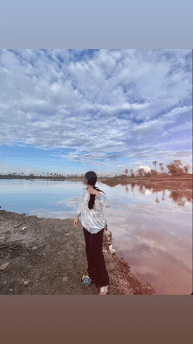 a woman stands on the shore of a lake with a blue sky in the background