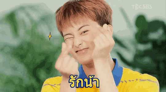 a young man in a yellow shirt is making a face with his hands