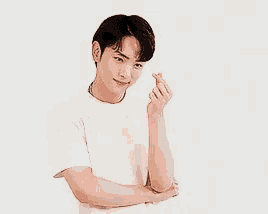 a young man in a white t-shirt is making a heart with his hands .