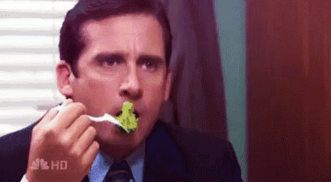 a man in a suit and tie is eating a spoonful of broccoli .
