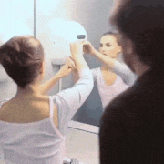 a woman is looking at herself in the mirror while a man looks on .