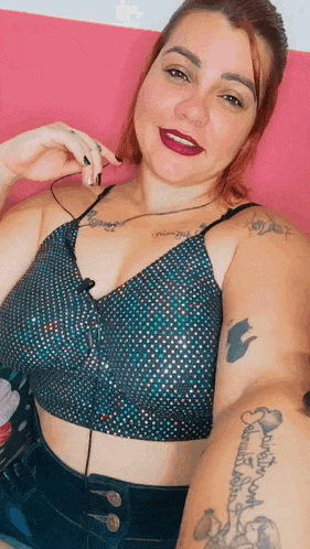 a woman with tattoos on her arm is taking a selfie while wearing a crop top and shorts .