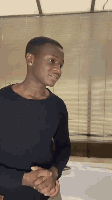 a young man in a black sweater is standing in front of a window