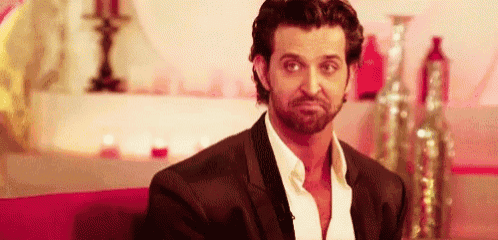 a man in a suit and white shirt is sitting on a couch making a face .
