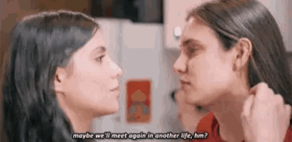 two women are looking at each other in a kitchen and talking .