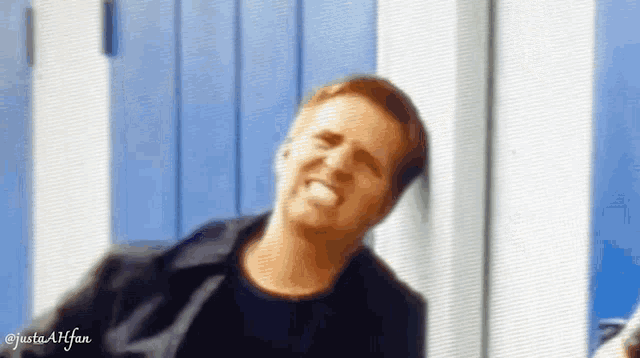 a man is leaning against a blue wall and smiling