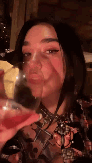 a woman in a plaid shirt is drinking from a wine glass