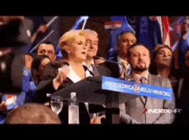a woman stands at a podium with a blue sign that says " presidencija "