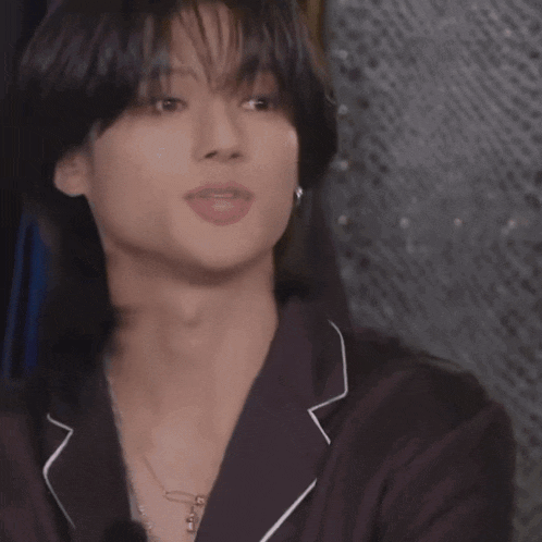 a close up of a young man wearing a necklace and a jacket
