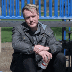 a man in a leather jacket is sitting on a blue bench holding a can of soda .