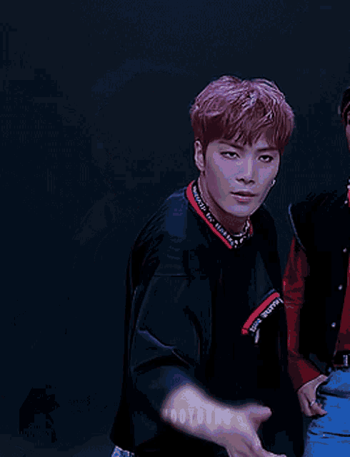 a young man with purple hair is wearing a black shirt with a red trim