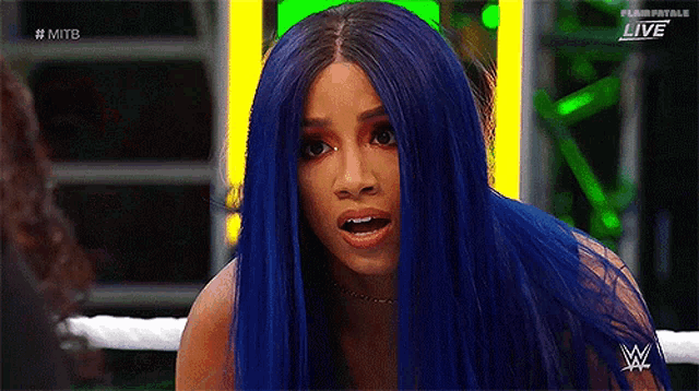 a woman with blue hair is standing in a wrestling ring and making a funny face .